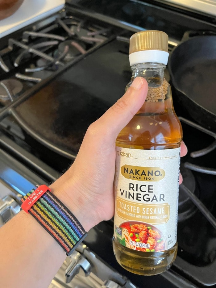 a person holding a bottle of rice vinegar in front of their stovetop