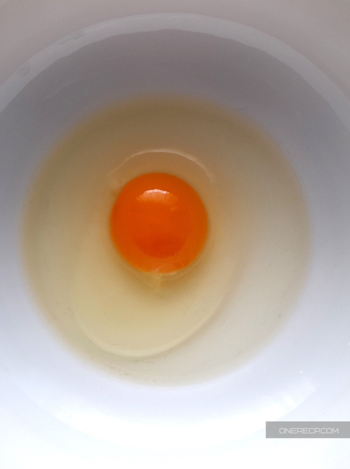 A raw egg without any signs of mold cracked on a white plate