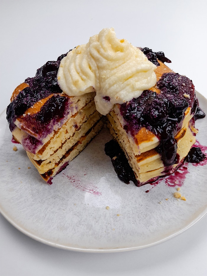 a plate with a stack of homemade protein powder pancakes with banana frosting and blueberry jam sliced so that the inside of the pancakes can be seen