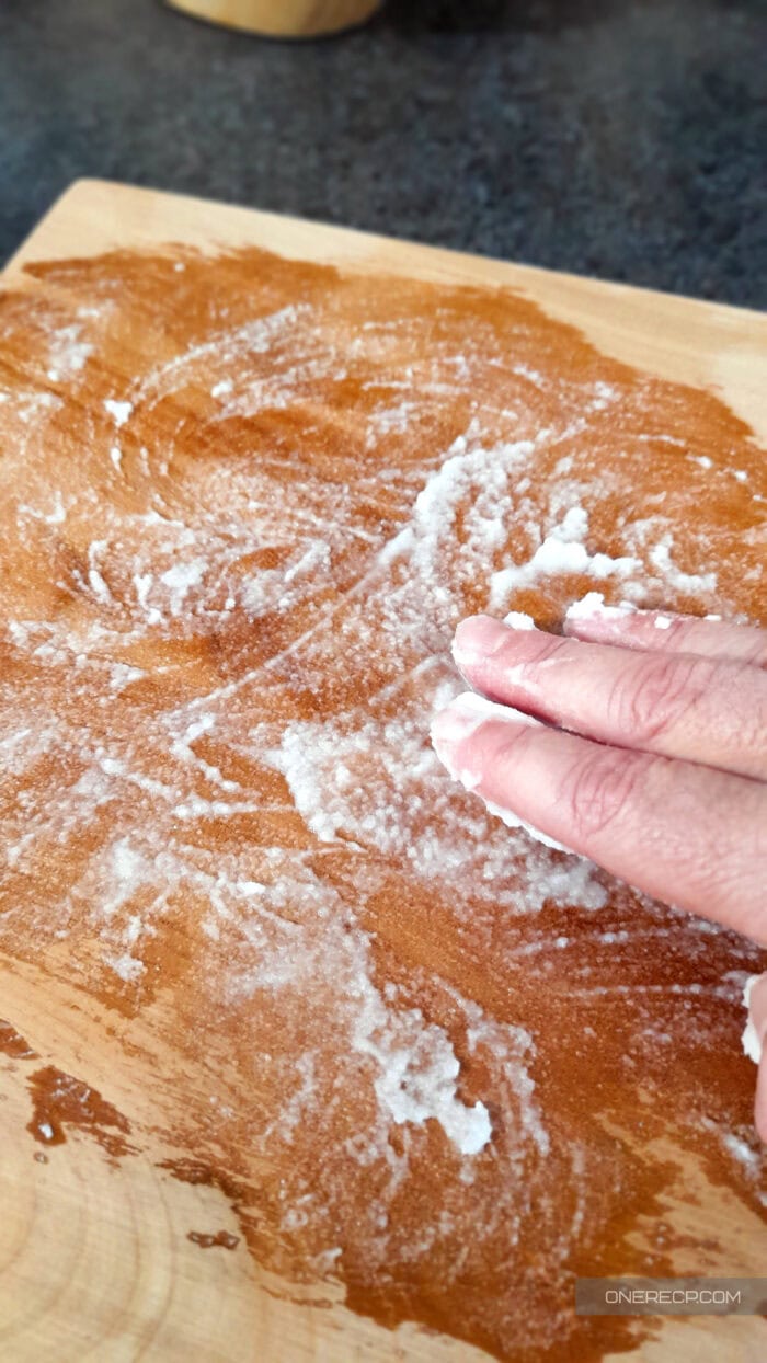 Person scrubbing a wooden cutting board with a baking soda paste for deep natural cleaning.