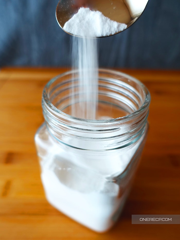 Baking soda poured out of a teaspoon into jar