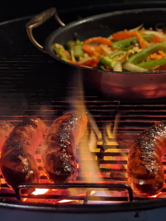 vienna sausages being barbecued next to a skillet full of grilled vegetables