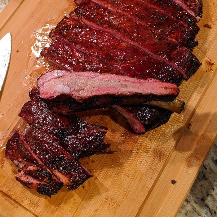 a rack of spare pork ribs smoked to perfection with one rib turned sideways so the smoke ring can be seen