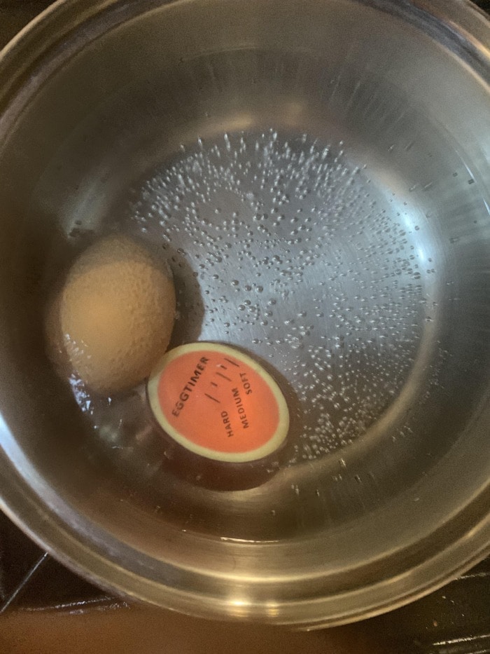 a special timer for boiled eggs sitting next to an egg in a pot with heated water