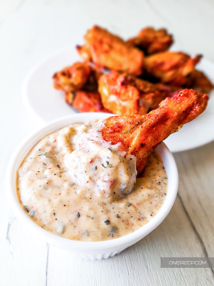Buffalo wild wings garlic parmesan sauce in a white sauce cup with a chicken wing dipped in it