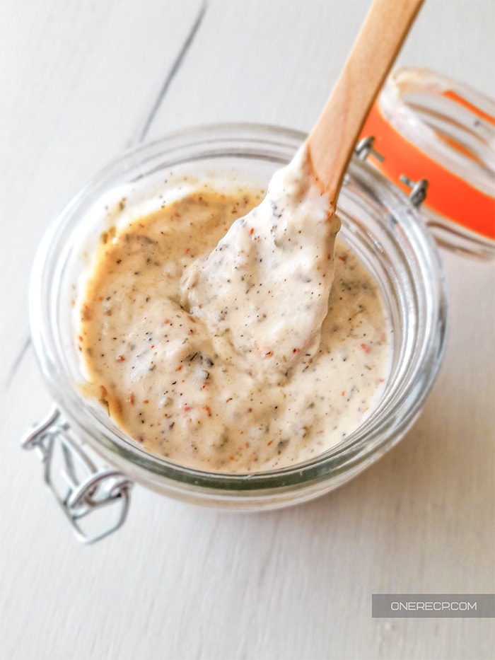 An opened jar with buffalo wild wings garlic parmesan sauce with a wooden spoon in it