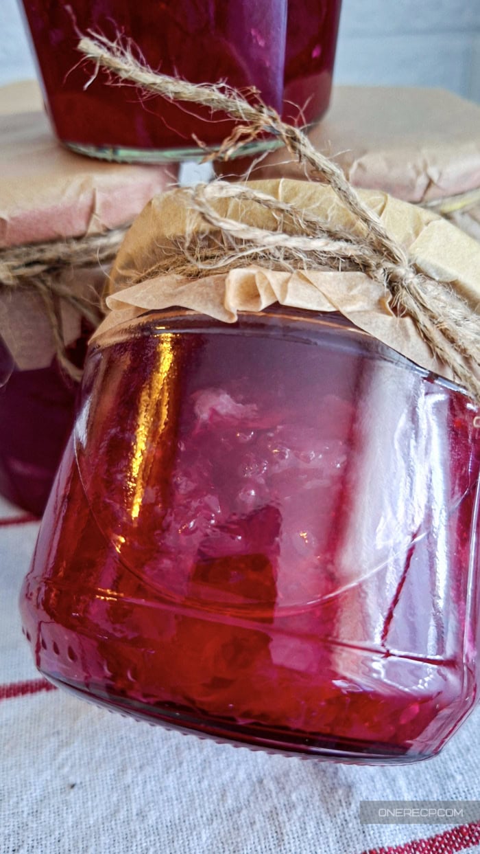 A glass jar filled with homemade Bulgarian rose petal jam, showcasing its vibrant ruby-red color and delicate rose petals suspended in syrup.