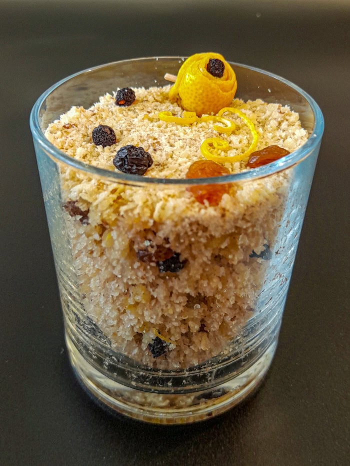 A glass filled with sweet bulgur wheat, garnished with raisins and lemon zest with a dark background