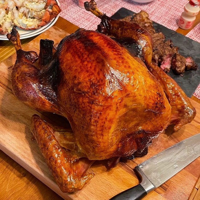 a whole cooked turkey on a wooden board with a knife next to it