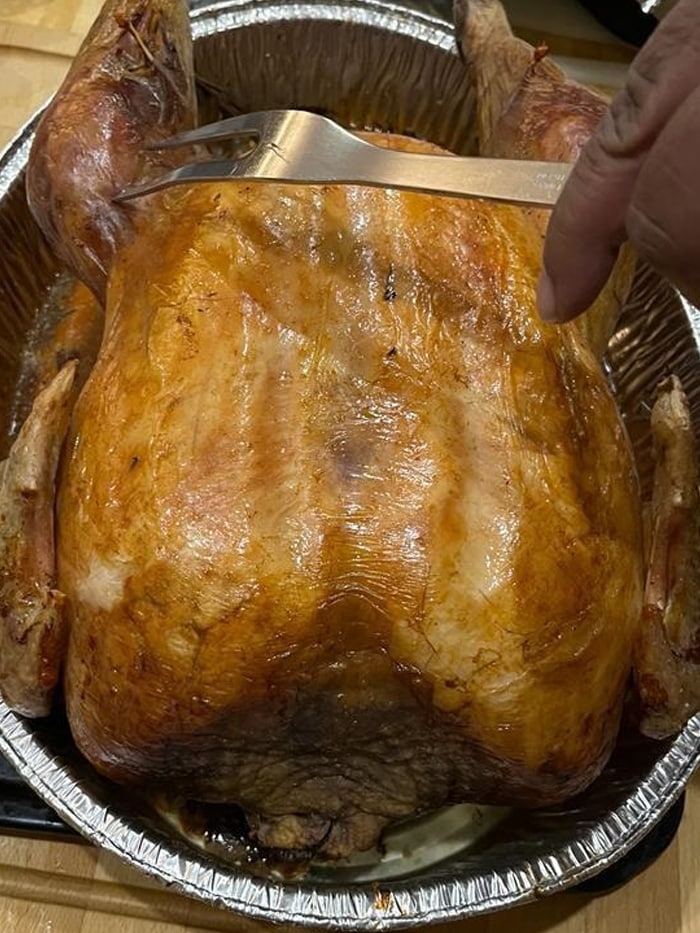 Sticking a fork in the thigh of a cooked turkey to check whether the meat is properly cooked