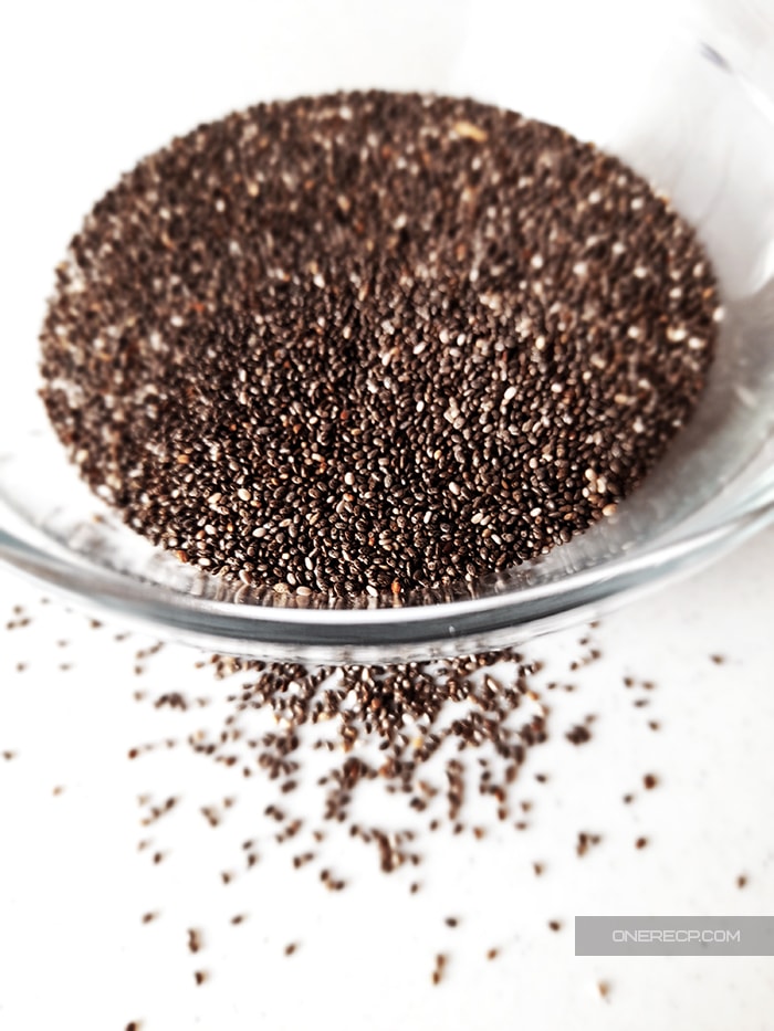 Chia Seeds in and in front of a glass cup on a white kitchen board