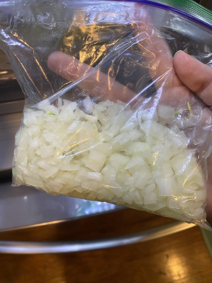 a hand holding a platic bag with chopped onions ready to be stored in the fridge