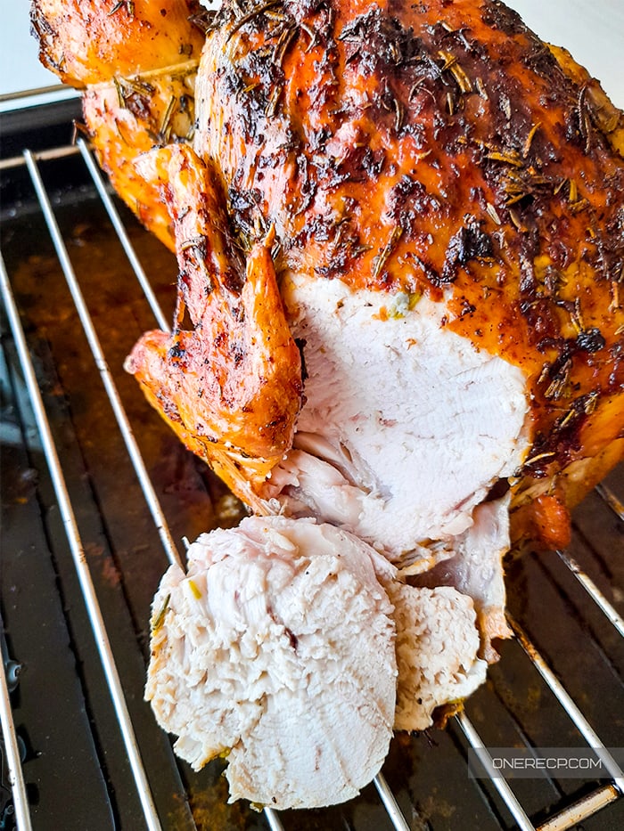 Convection-roasted whole chicken on a baking rack with a sliced piece off its breasts