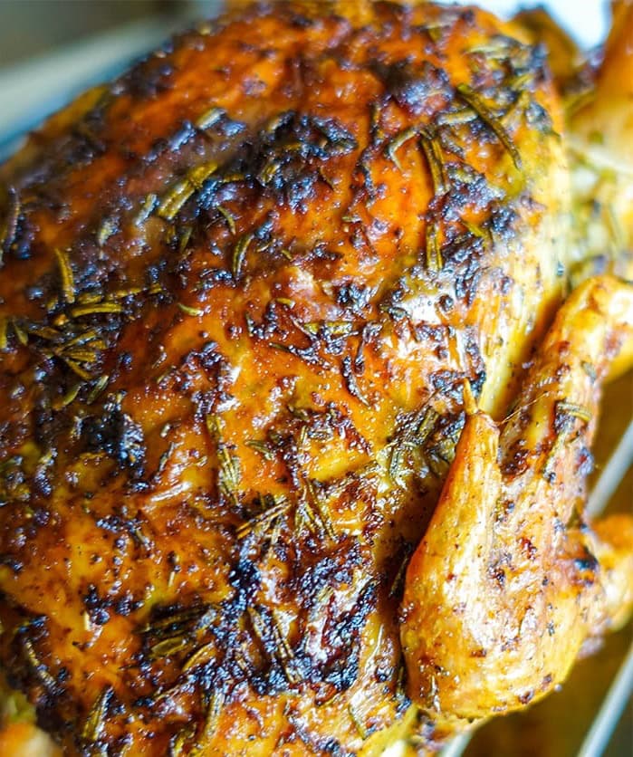 a close up of a whole roasted chicken with butter showing the cripsy texture of the baked skin and the herbs