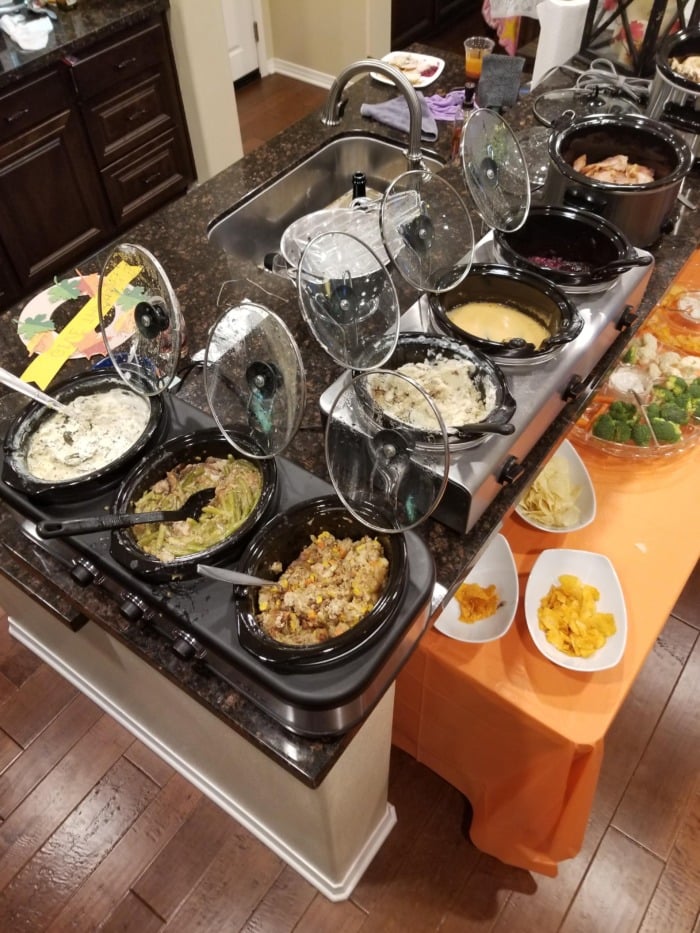 Six crockpots on a kitchen isle keeping meals warm for a family gathering on Thanksgiving