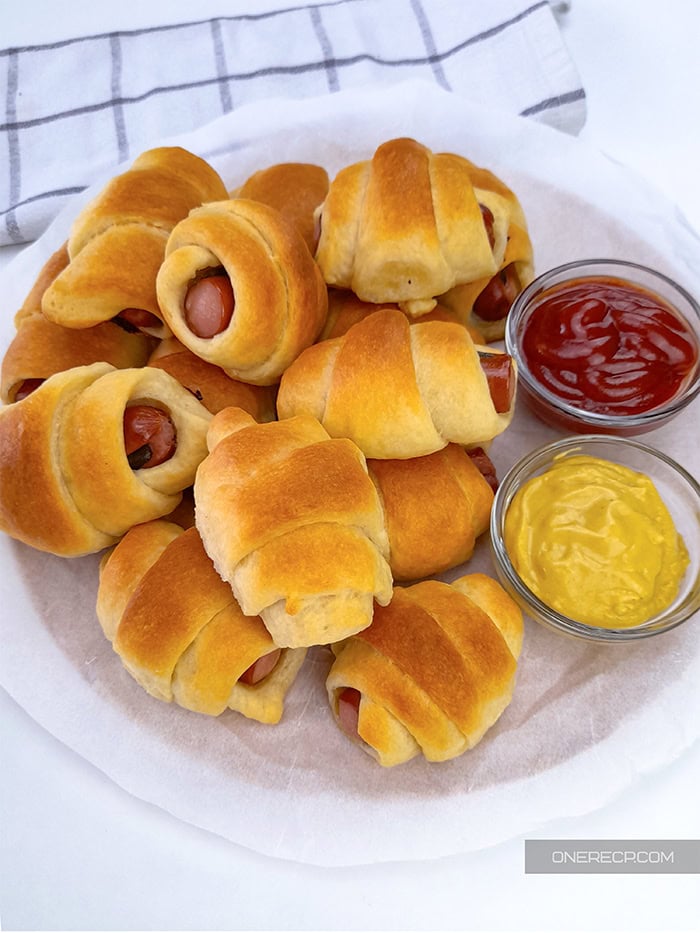 Crescent pigs in a blanket served with mustard and ketchup.