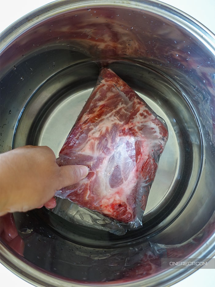 Placing frozen pork shoulder in a large bowl filled with cold water