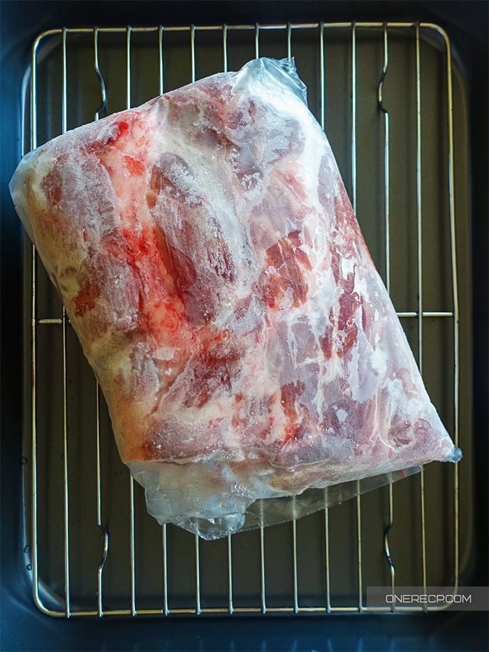 Frozen pork shoulder on a wire rack, prepared for defrosting in the fridge