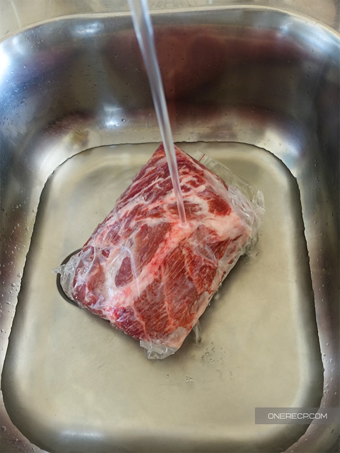 Frozen pork shoulder in a kitchen sink under running water