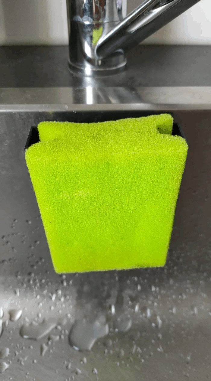 A bright green kitchen sponge drying upright on a sink holder to prevent moisture buildup and bad smells.