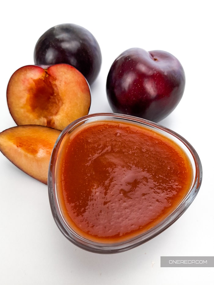 a small bowl holding the BBQ sauce with whole and chopped in half plums in the back