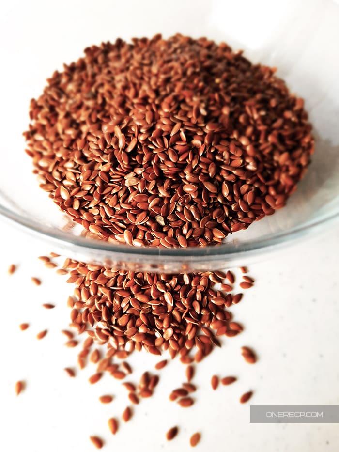 Flax seeds in and in front of a glass cup on a white kitchen board