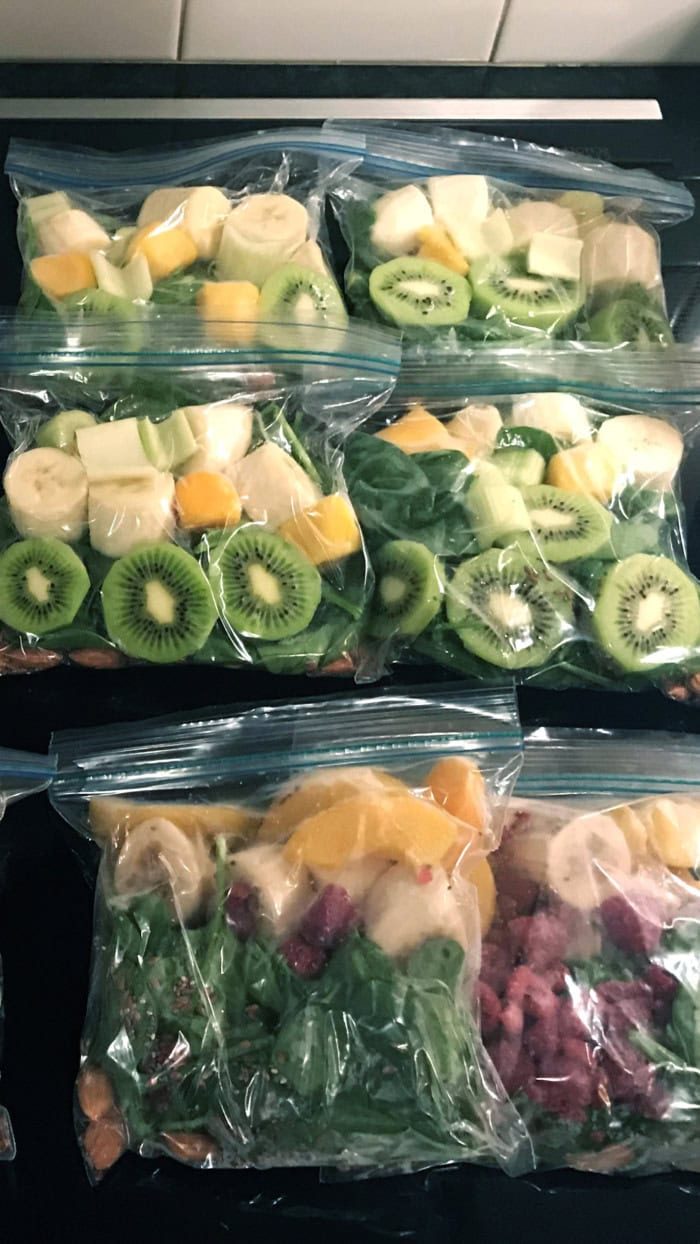 Freezer smoothie packs filled with spinach, banana, kiwi, and frozen fruit prepared in zip-top bags for quick make-ahead smoothies.