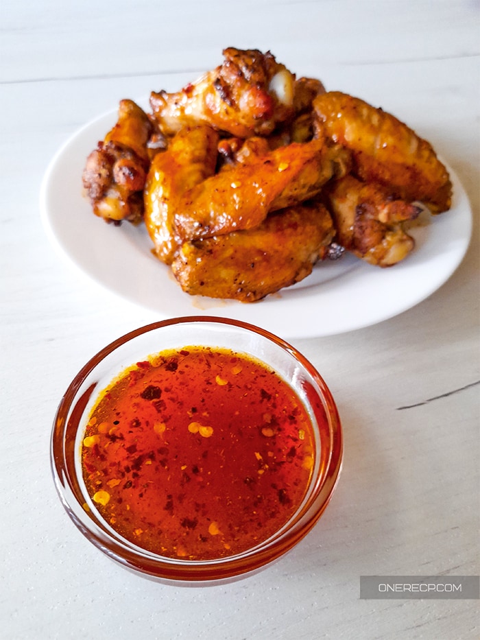 Hot Honey wing sauce in a small glass cup with chicken wings in the background