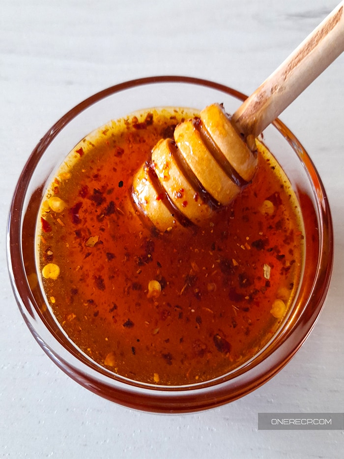 A sauce glass cup of honey hot wing sauce with a honey dipper in it