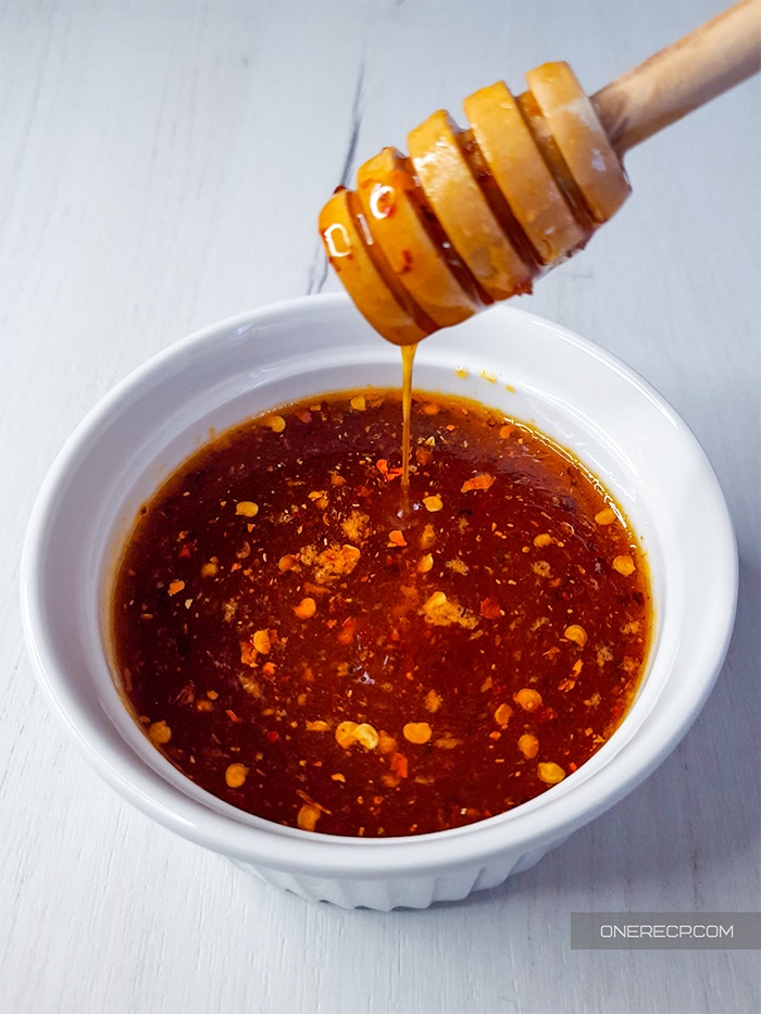 Honey dipper above a white cup with honey hot wing sauce