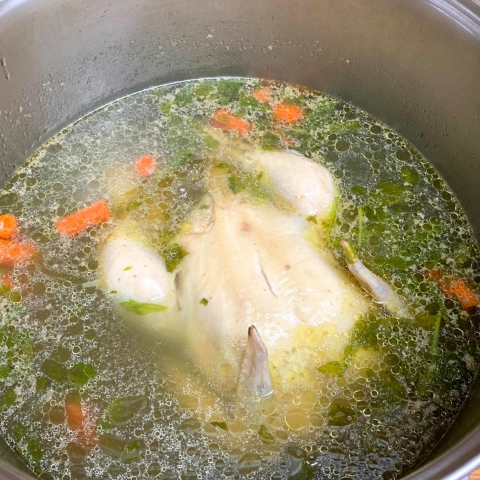 a whole chicken being boiled in a pot with seasonings and some vegetables