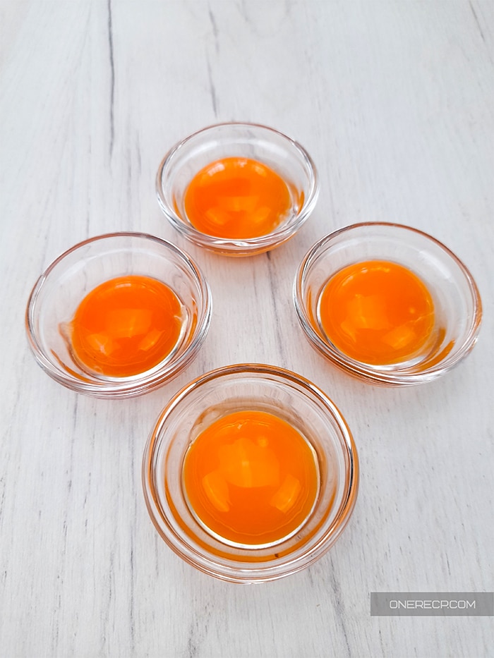 four individual small glass bowls holding one egg yolk each