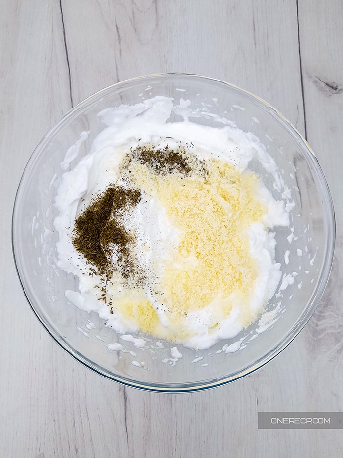 A glass bowl with beat egg whites, sprinkled parmesan cheese and spices 