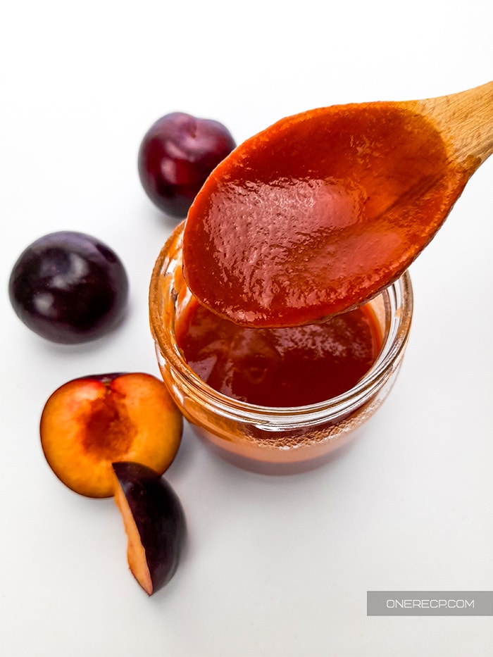 transfering the BBQ sauce in a small jar with a wooden spoon and a couple of plums in near the jar