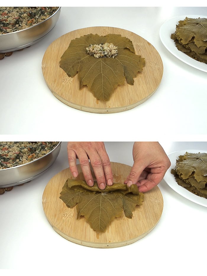 Spreading rice over a grape leaf and rolling the leaf over a cutting board