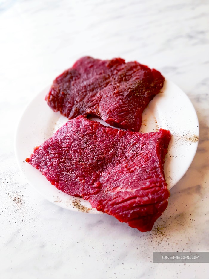 Two raw seasoned cube steaks on a white plate