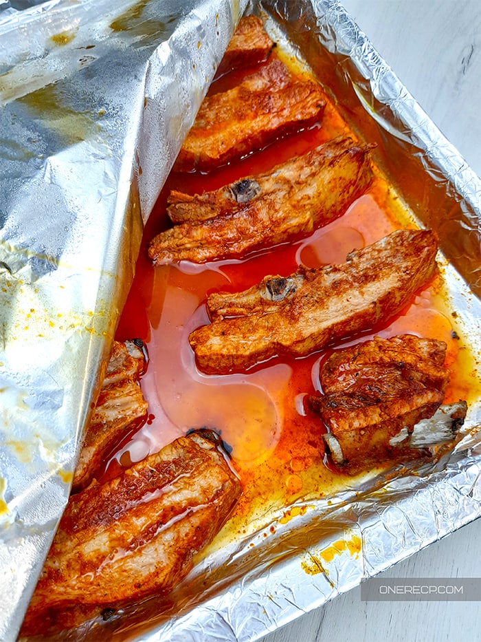Taking off aluminum foil from baking dish with roasted pork ribs