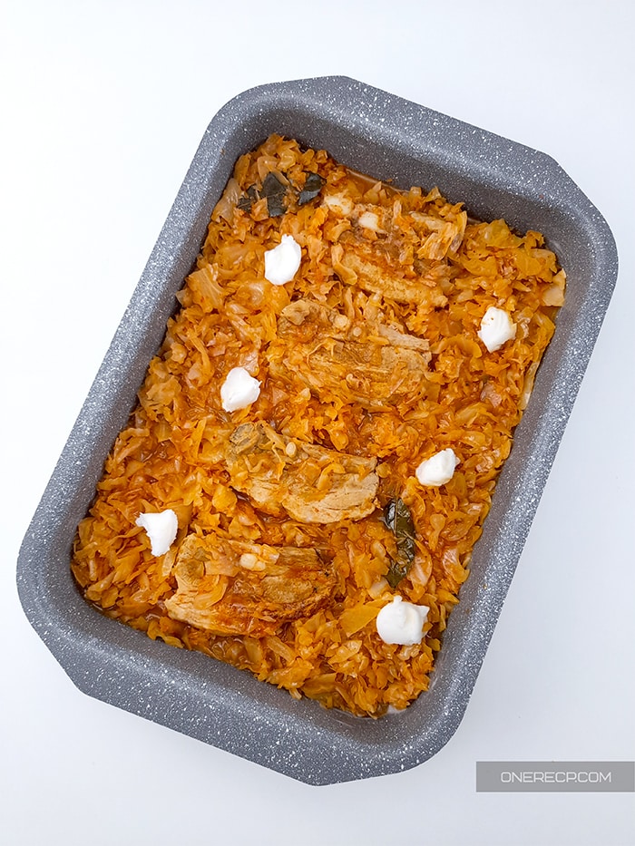 A baking dish with partially cooked pork and sauerkraut and some pork lard on top