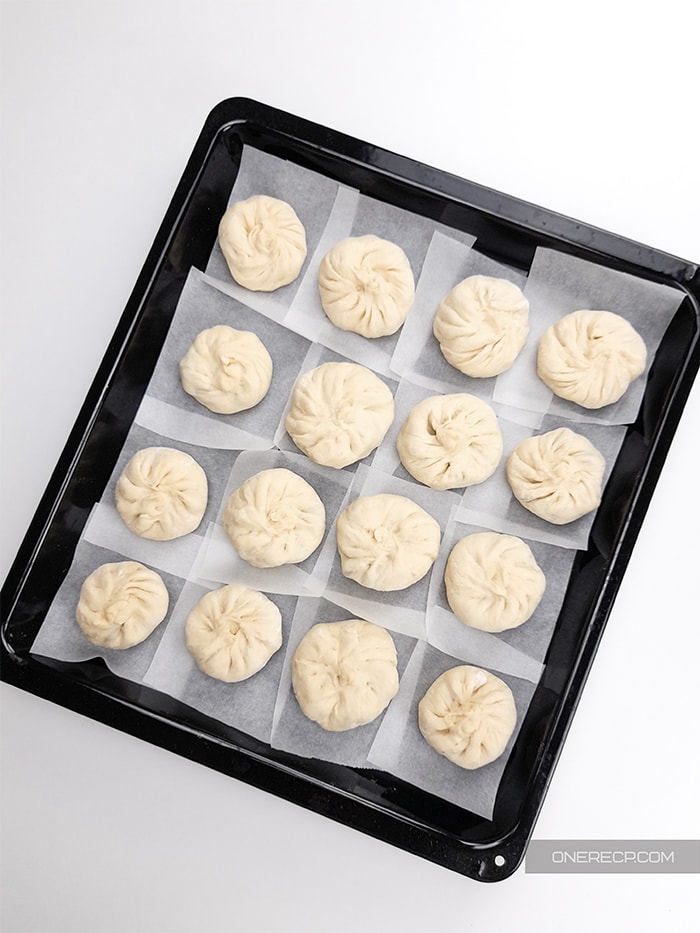 a pan with individual parchment paper sheets holding the sealed pork buns