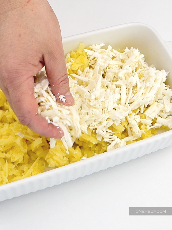 Covering shredded potatoes with feta cheese