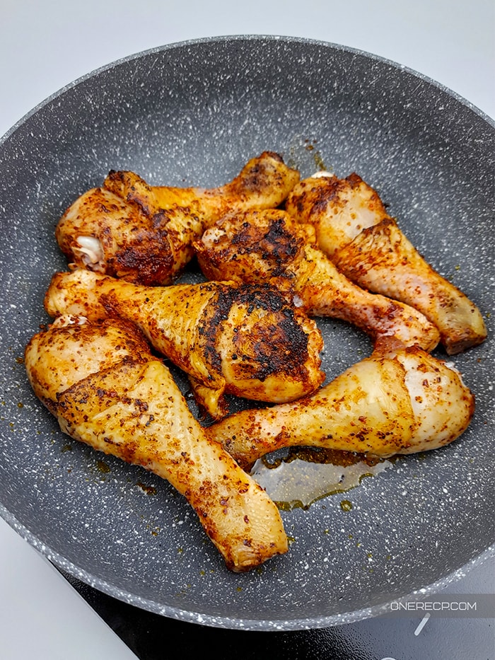 six chicken drumsticks with crispy skin in a frying pan being done and ready to take off the stove top