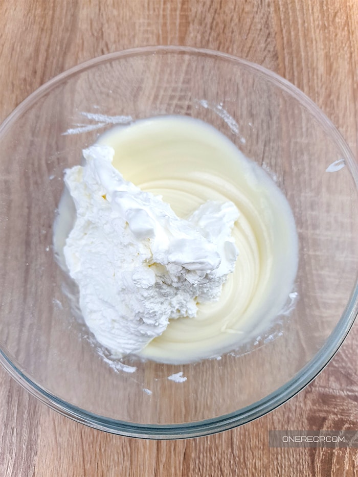 a glass bowl of beat cream cheese with added whipped heavy cream