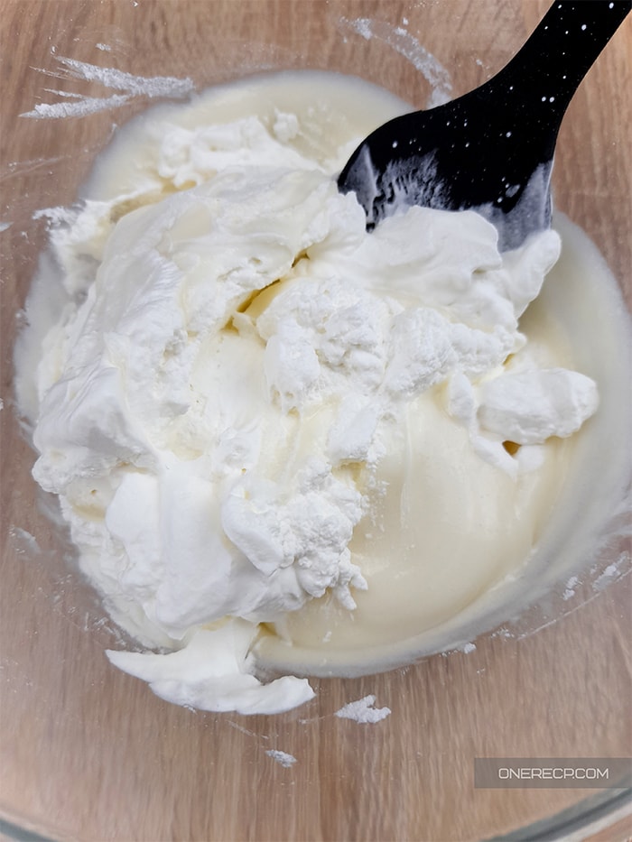 folding the heavy cream into the beat cream cheese with a spatula in a glass bowl