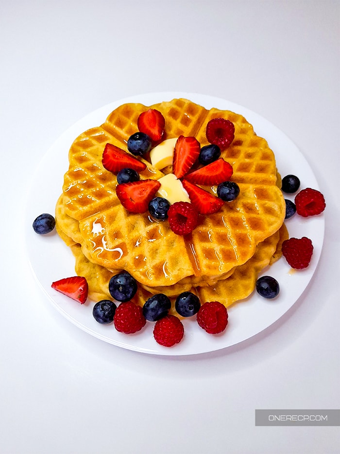 Top view of stack of waffles garnished with strawberries, raspberries, and blueberries in a plate