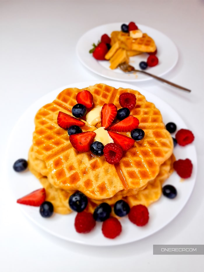 Waffles served with a piece of butter, maple syrup, and fresh fruits