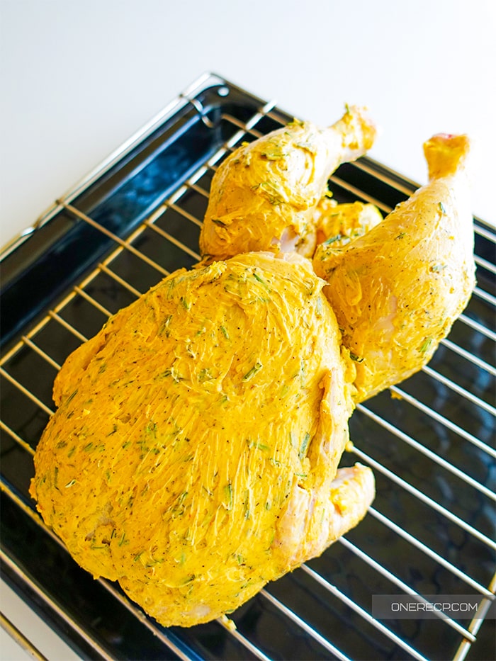 A whole chicken covered with butter and herbs on a baking rack