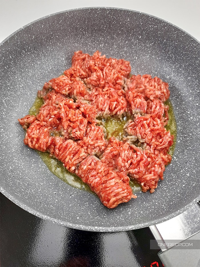 Ground beef being cooked in a pan with olive oil