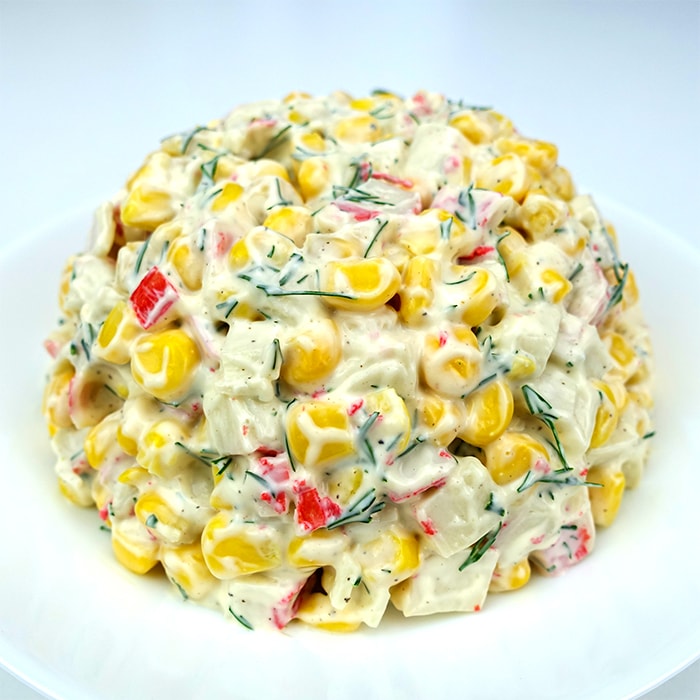 a plate with a ball-shaped serving of imitation crab salad with corn and mayonnaise