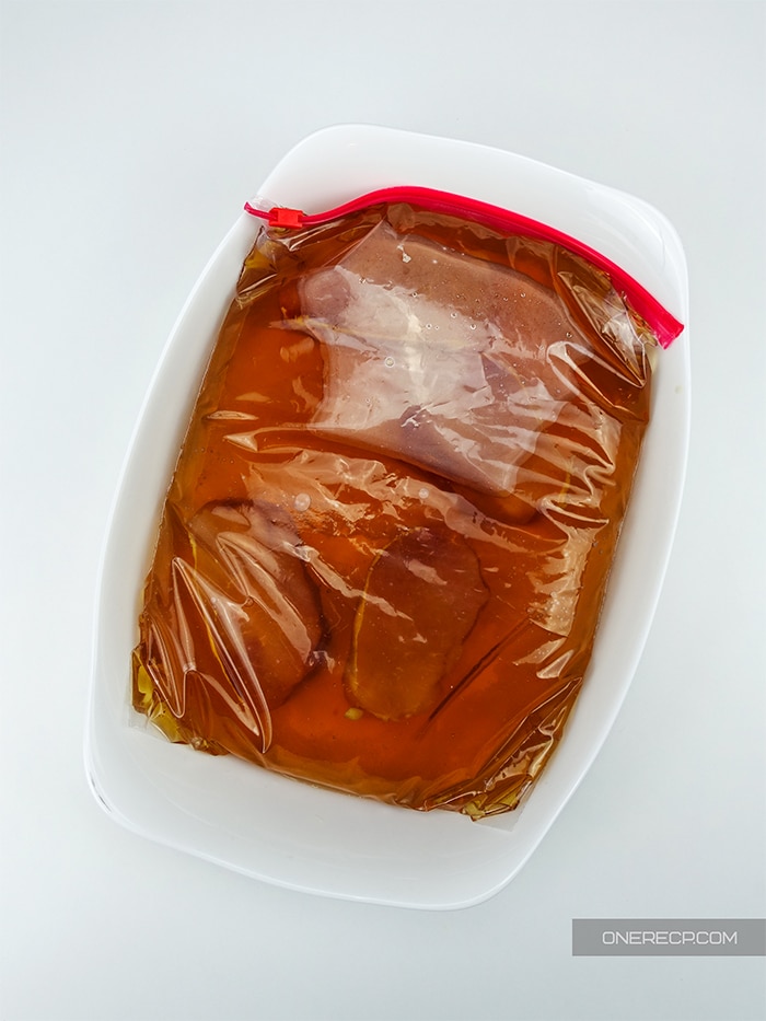 a bowl holding raw pork chops in a ziploc bag with marinade 