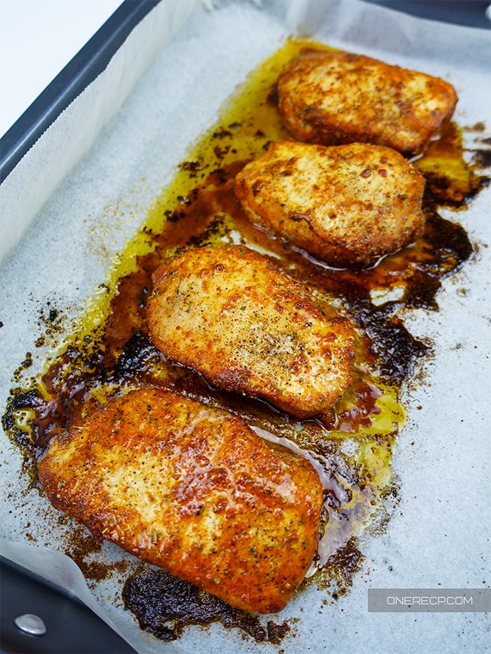 four sizzling oven baked pork chops lying in a baking tray 